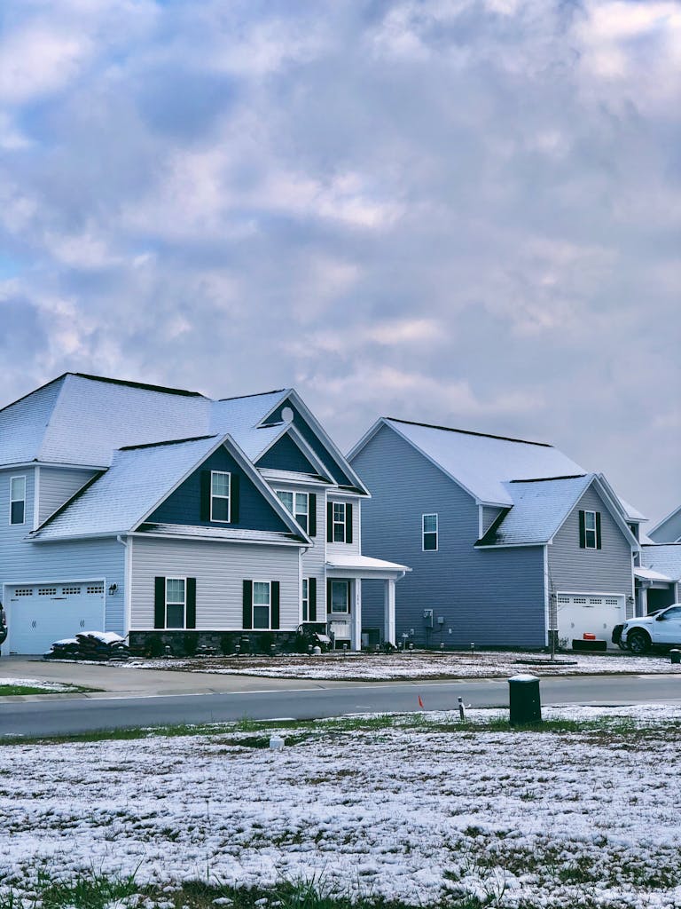 Charming suburban homes with light snow on rooftops and ground, cloudy winter sky overhead.